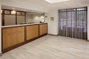 Zona de recepción de un hotel con un mostrador de madera, una barra y un amplio ventanal con cortinas.
