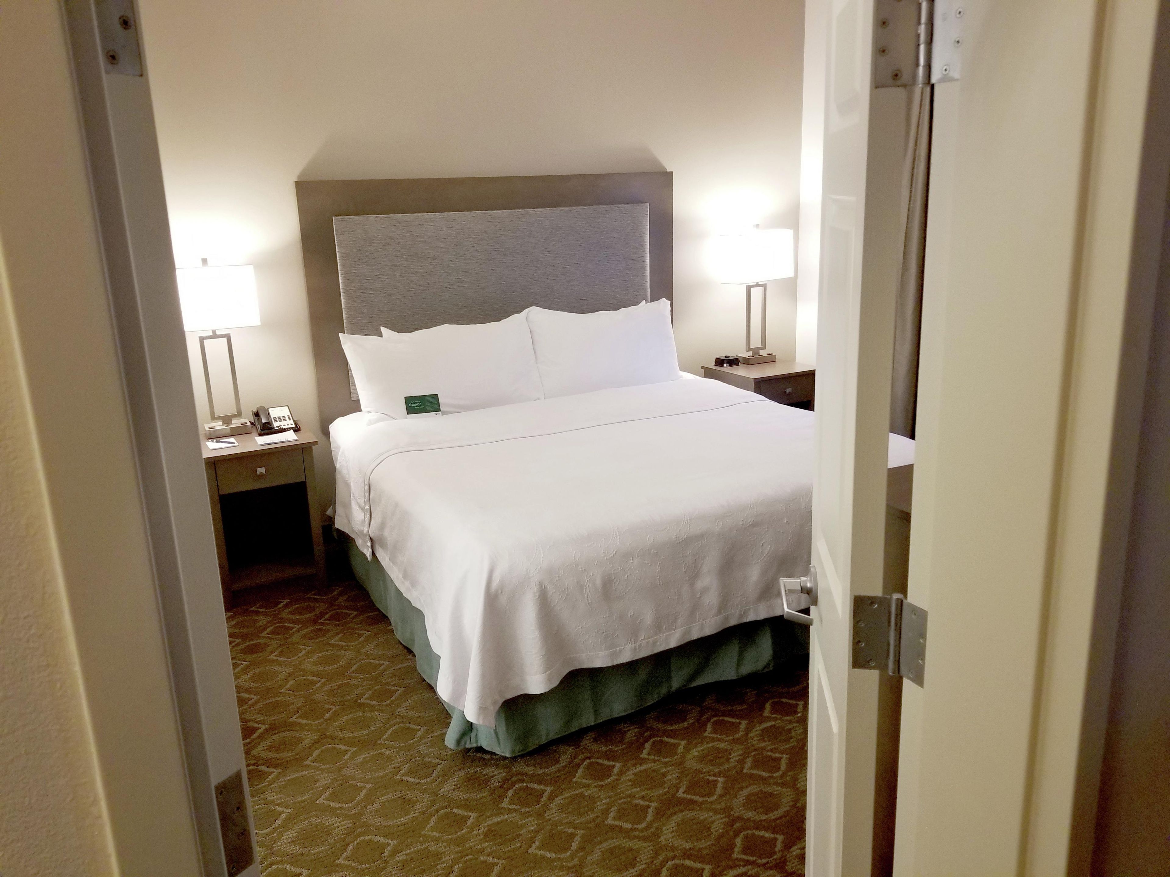 A hotel room with a bed, bedside tables, a lamp, and a carpeted floor.