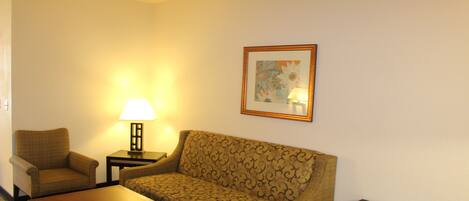 A hotel room with a patterned sofa, a small table, a lamp, and a framed picture on the wall.