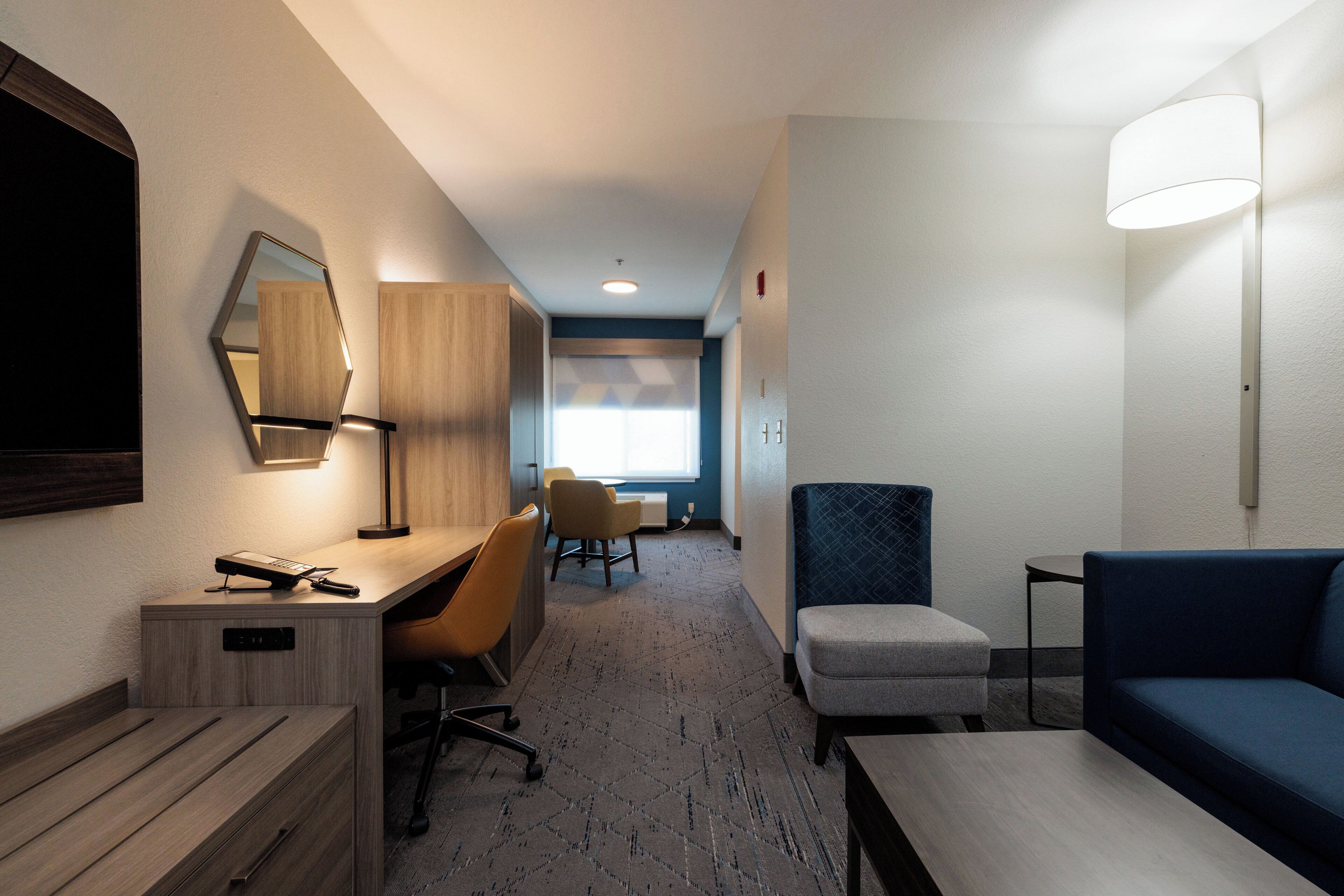A hotel room with a desk, chair, sofa, and a large mirror.