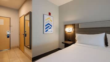 A hotel room with a bed, a nightstand, a wall-mounted light, a door, and a framed picture.