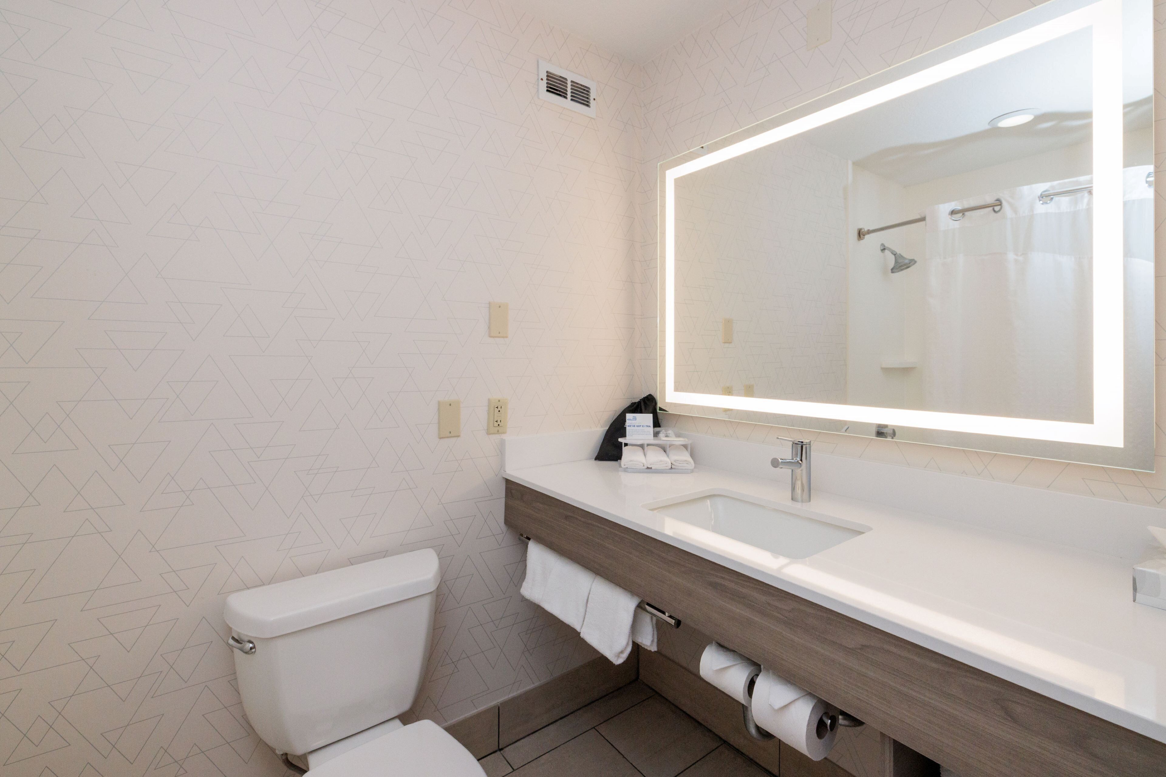 Un baño moderno con inodoro blanco, tocador de madera con lavamanos y un espejo grande.