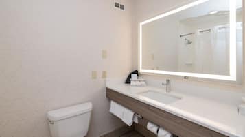 Un baño moderno con inodoro blanco, tocador de madera con lavamanos y un espejo grande.