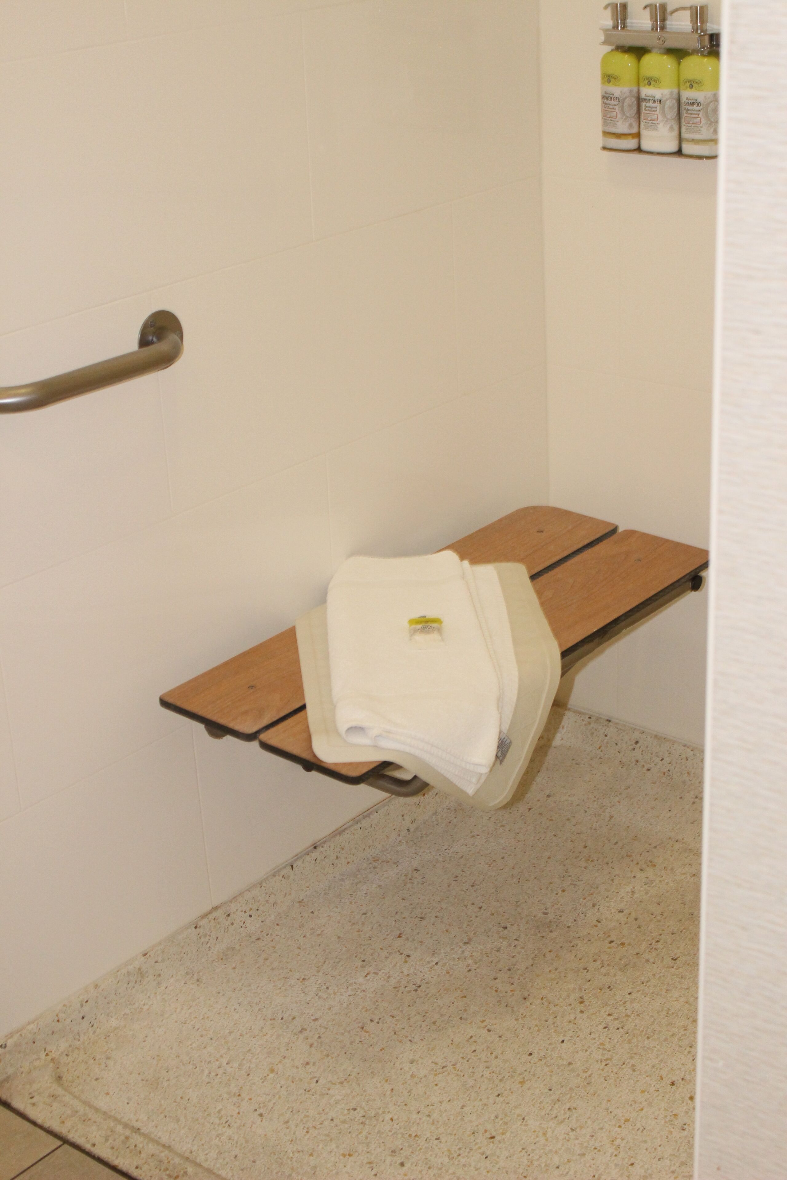 A bathroom with a shower, a bench, and a shelf with toiletries.