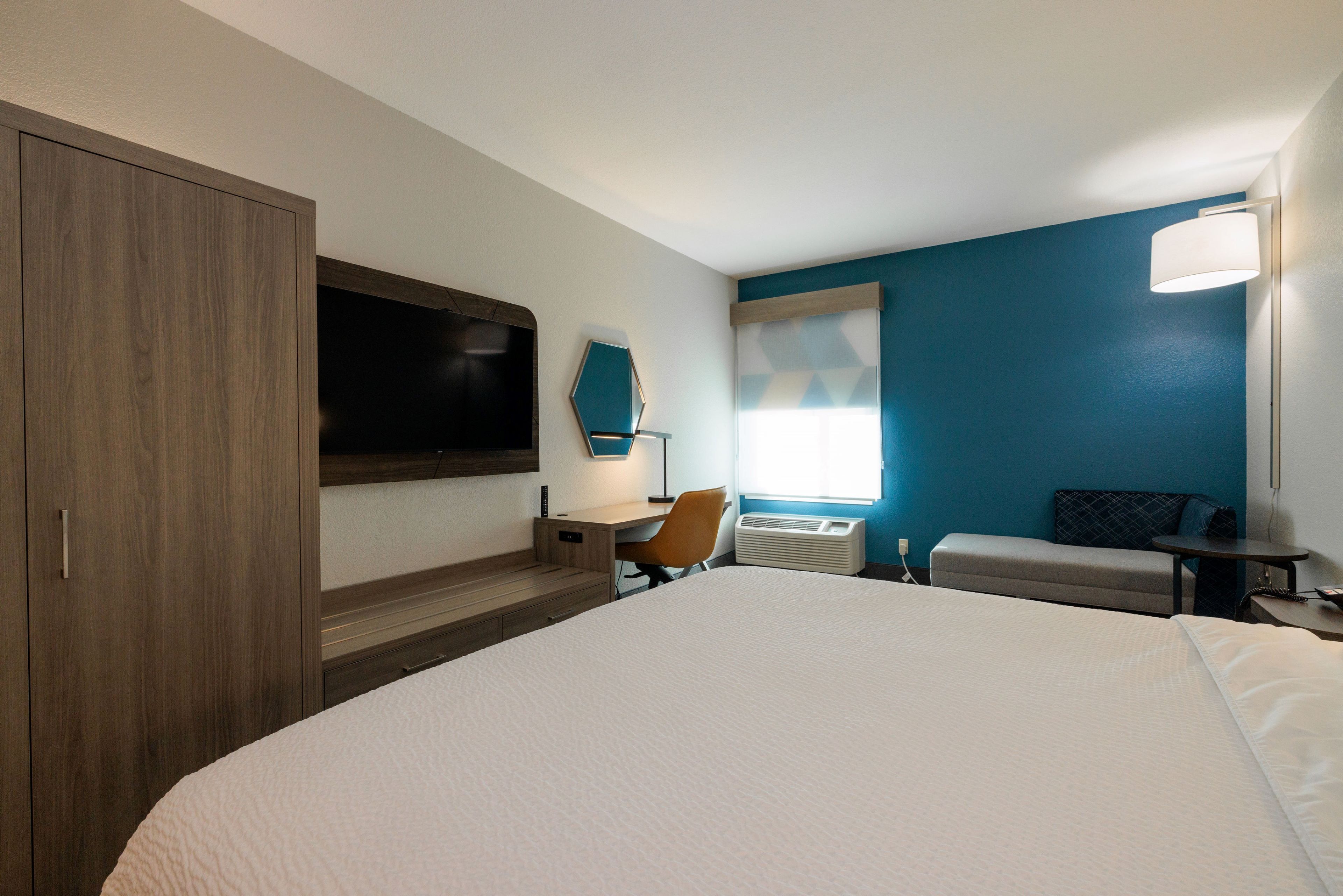 Hotelkamer met een groot bed, een bureau, een stoel, een televisie, een raam met zonwering en een wandlamp.