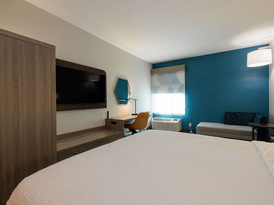 Hotelkamer met een groot bed, een bureau, een stoel, een televisie, een raam met zonwering en een wandlamp.