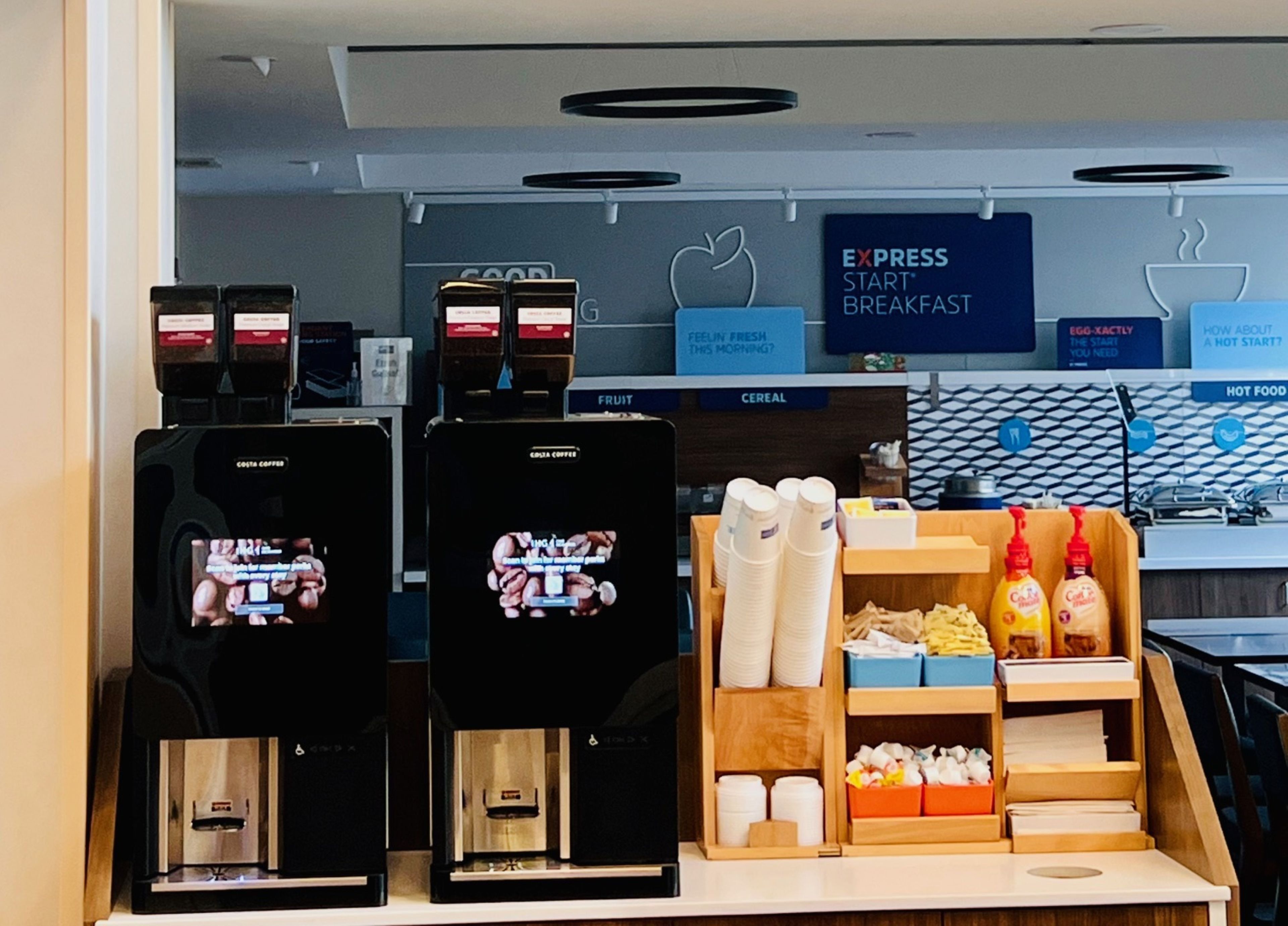 A coffee station with branded coffee machines, a sign for 'EXPRESS START BREAKFAST', and a variety of breakfast items.