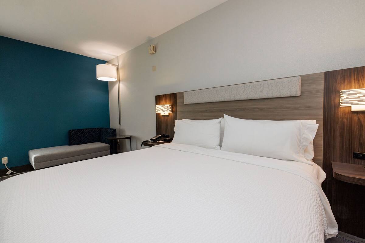 A hotel room with a large bed, a bench, a nightstand, and a wall-mounted lamp.