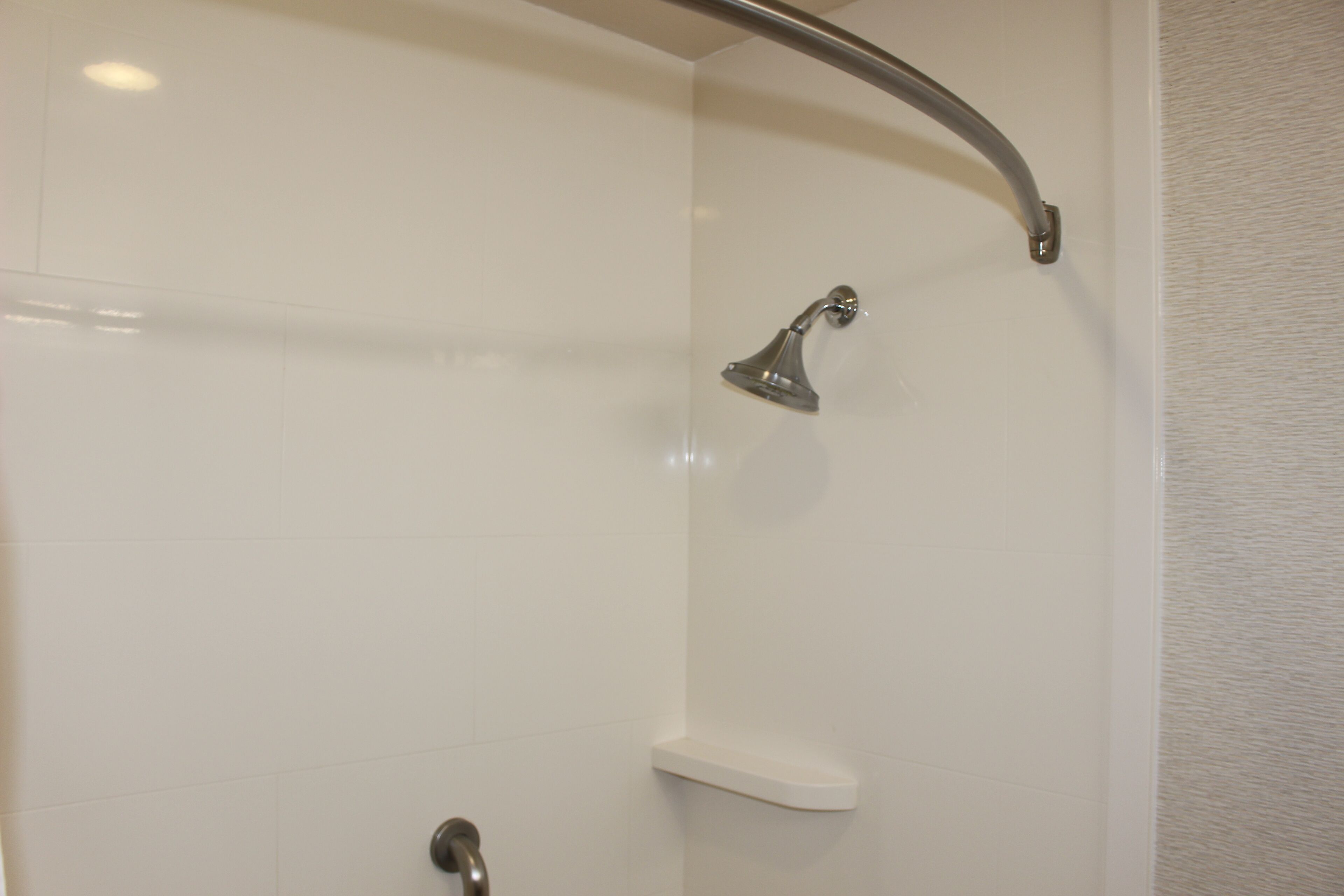Une douche dotée d’une poignée en métal incurvée et d’un pommeau de douche amovible.