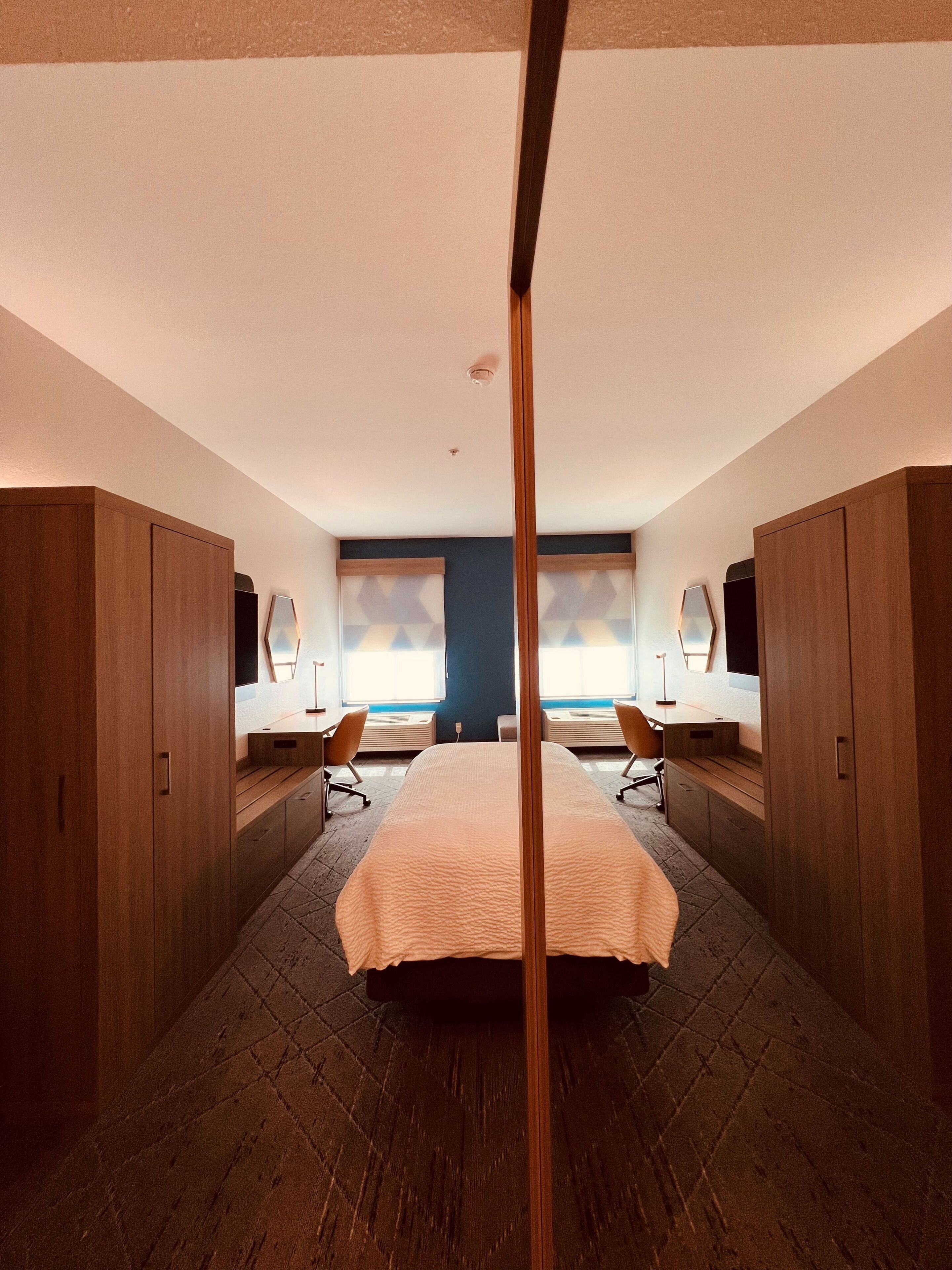 Ein modernes Hotelzimmer mit einem großen Bett, einem Holzschrank und Blick auf die Stadt durch die Fenster.
