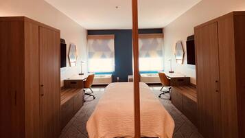 Ett modernt hotellrum med en stor säng, ett träskåp och utsikt över staden genom fönstren.