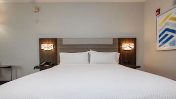 Een hotelkamer met een groot bed, twee nachtkastjes met lampen, een houten hoofdeinde en een gekaderd abstract kunstwerk aan de muur.