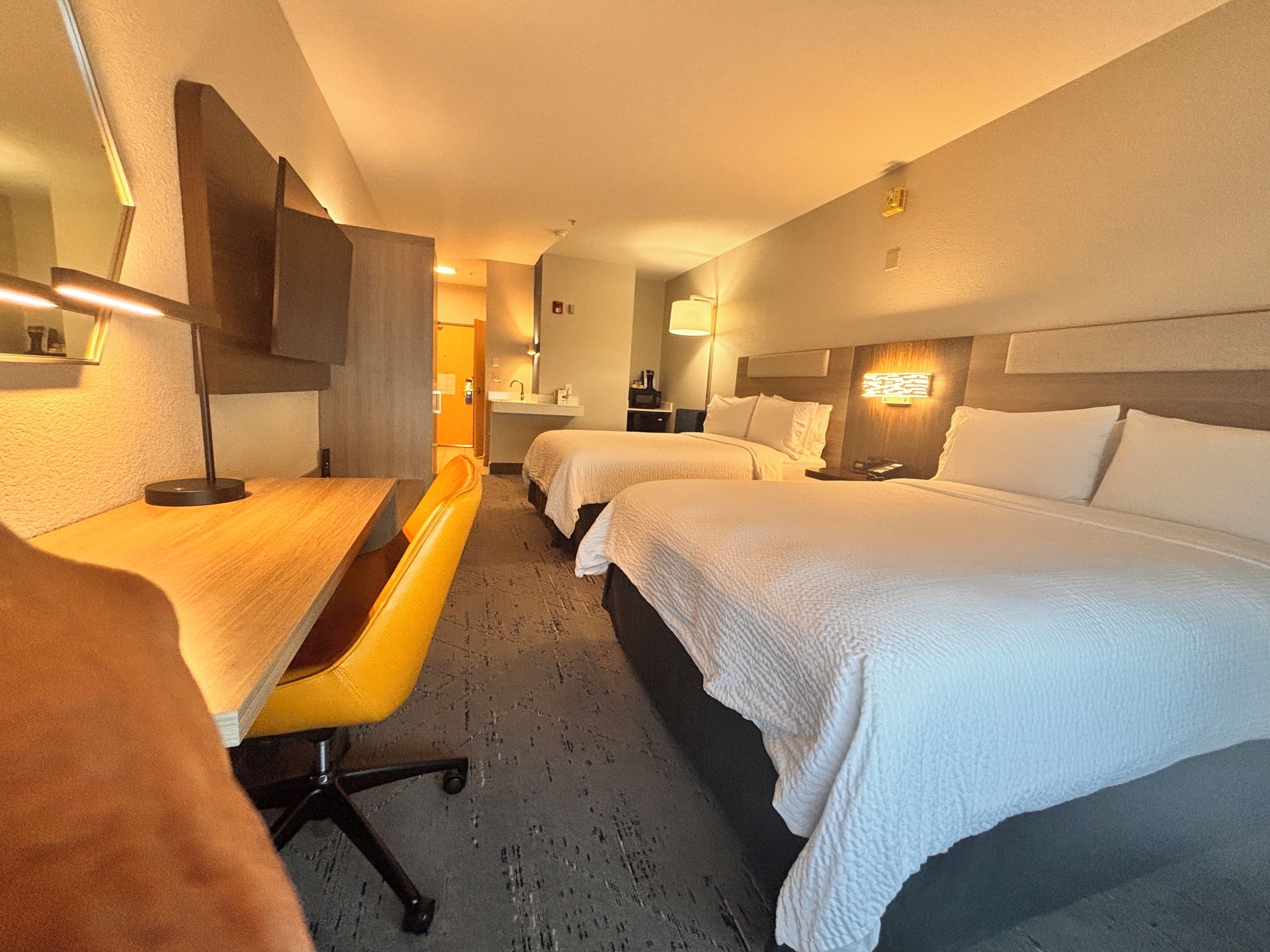 A hotel room with two beds, a desk, a chair, and a bathroom visible in the background.