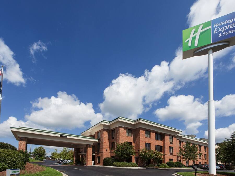 A Holiday Inn Express & Suites hotel with a brick facade, a covered parking area, and a clear blue sky with clouds.