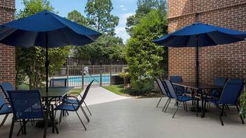 An outdoor patio area with a pool, brick walls, and blue umbrellas providing shade.