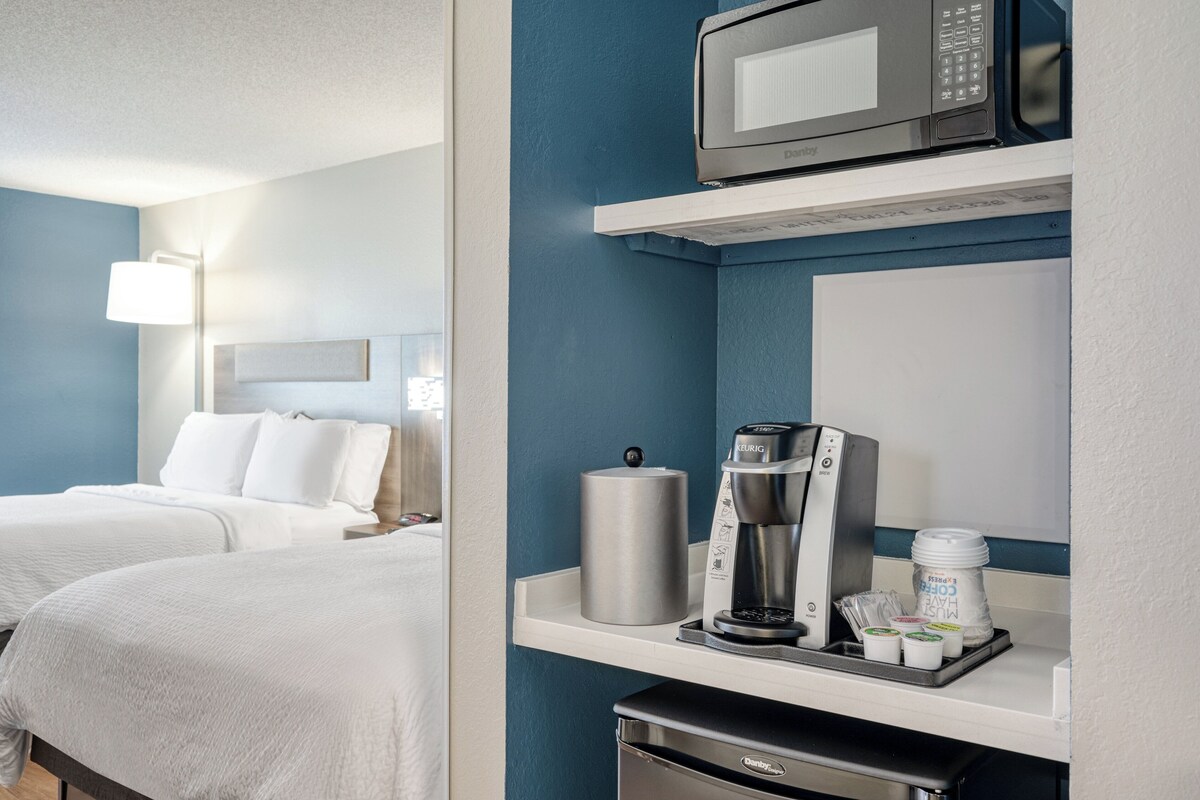 Quarto de hotel com duas camas, micro-ondas, cafeteira e um pequeno frigorífico.