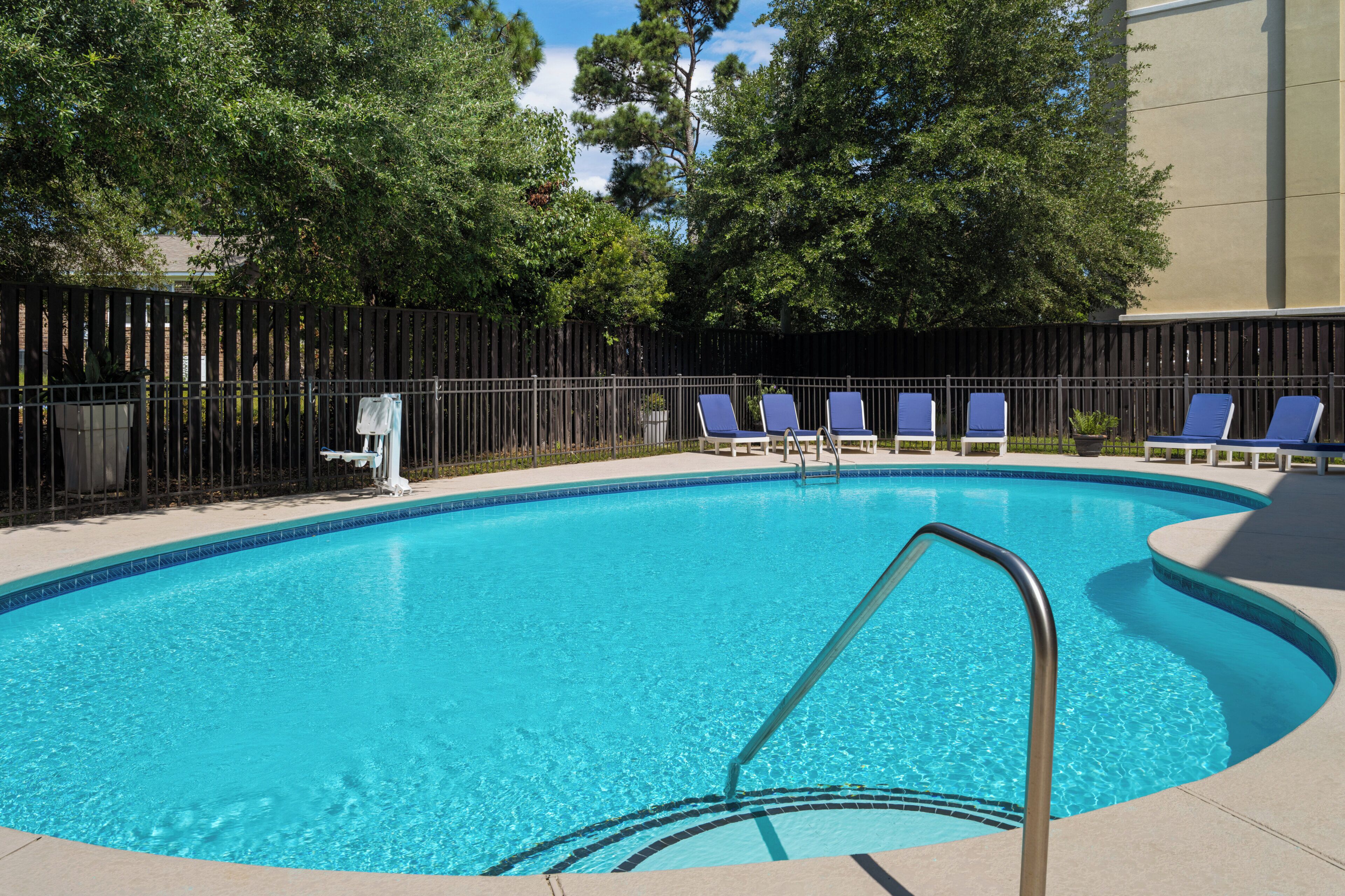 A swimming pool with a metal ladder, surrounded by a black fence and trees.