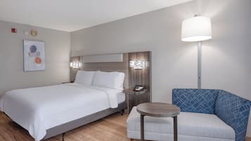 Una habitación de hotel con cama, mesita de noche, lámpara, silla y una obra de arte en la pared.