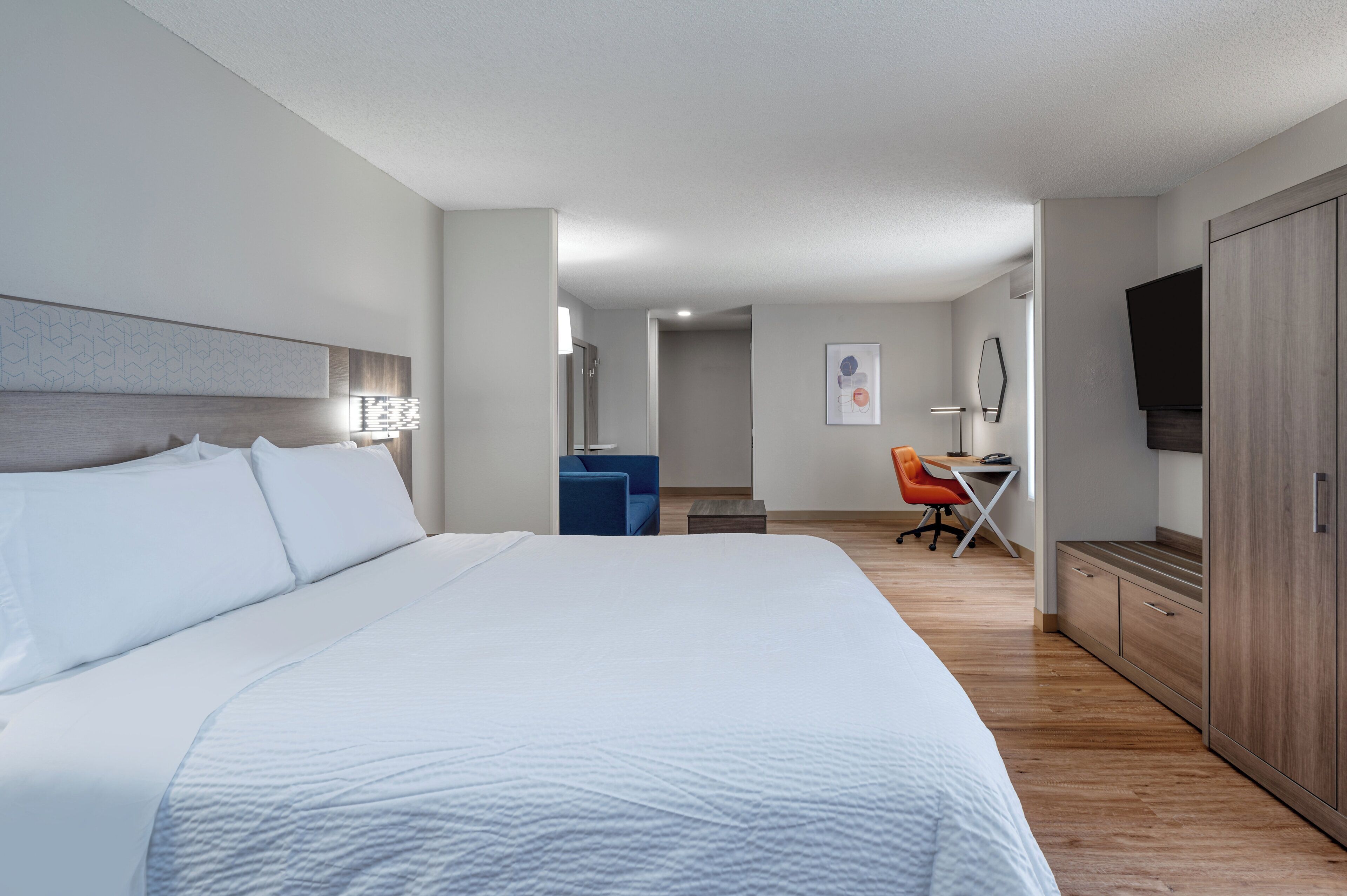 A hotel room with a large bed, a desk, a chair, and a TV.