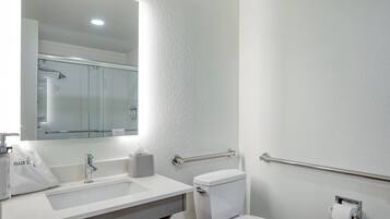 Baño con lavamanos blanco, espejo, inodoro y barras de apoyo.