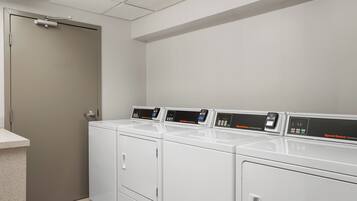A laundry room with four white front-loading washers and dryers, a door, and a countertop.