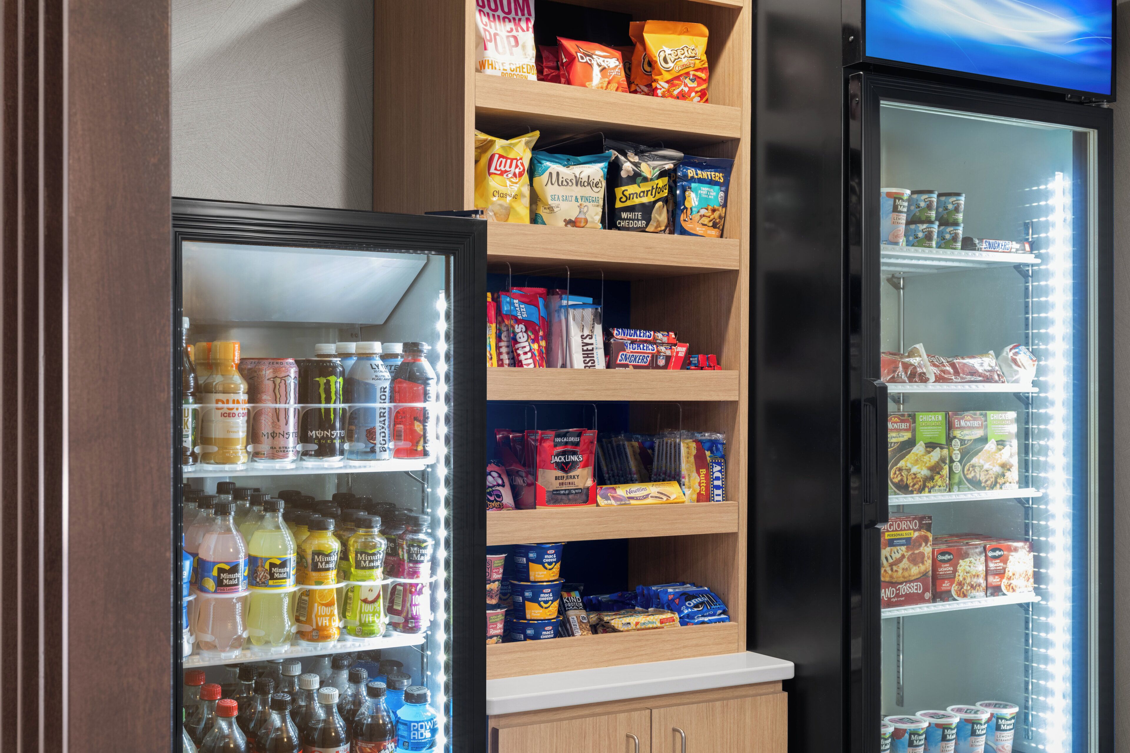 A vending machine stocked with snacks and drinks, a refrigerated display case with beverages, and a shelf with packaged food items.