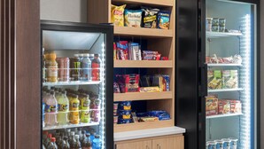 A vending machine stocked with snacks and drinks, a refrigerated display case with beverages, and a shelf with packaged food items. - Holiday Inn Express & Suites Columbia-I-20 @ Clemson Rd by IHG (Columbia)