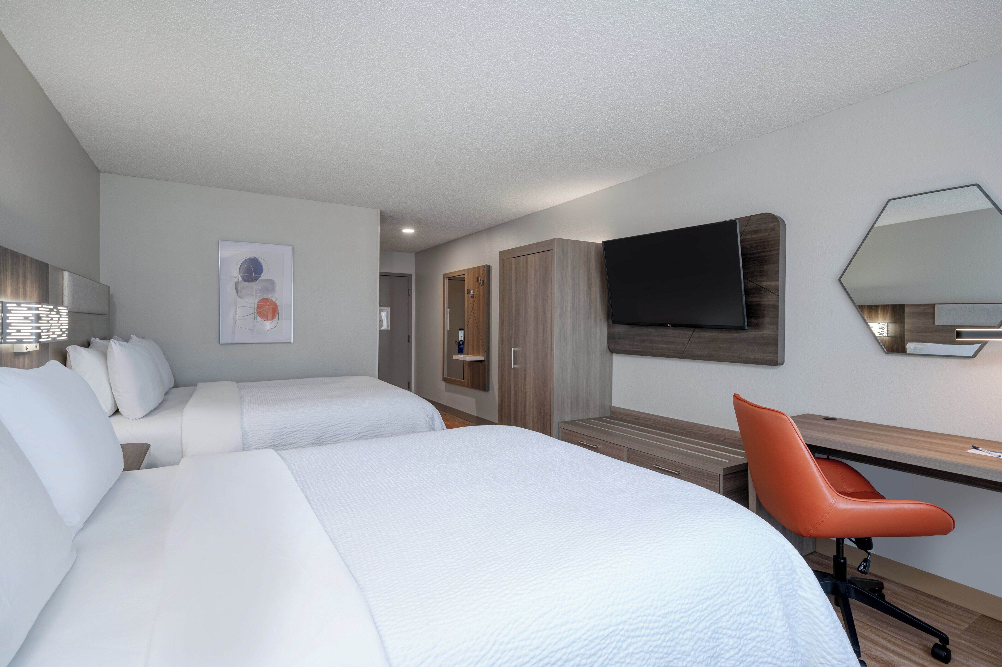 A hotel room with two beds, a desk, a chair, a TV, and a wardrobe.