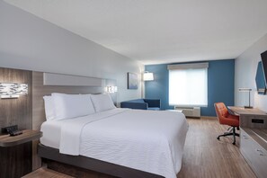 Ein Hotelzimmer mit Bett, Nachttisch, Schreibtisch, Stuhl und einem großen Fenster.