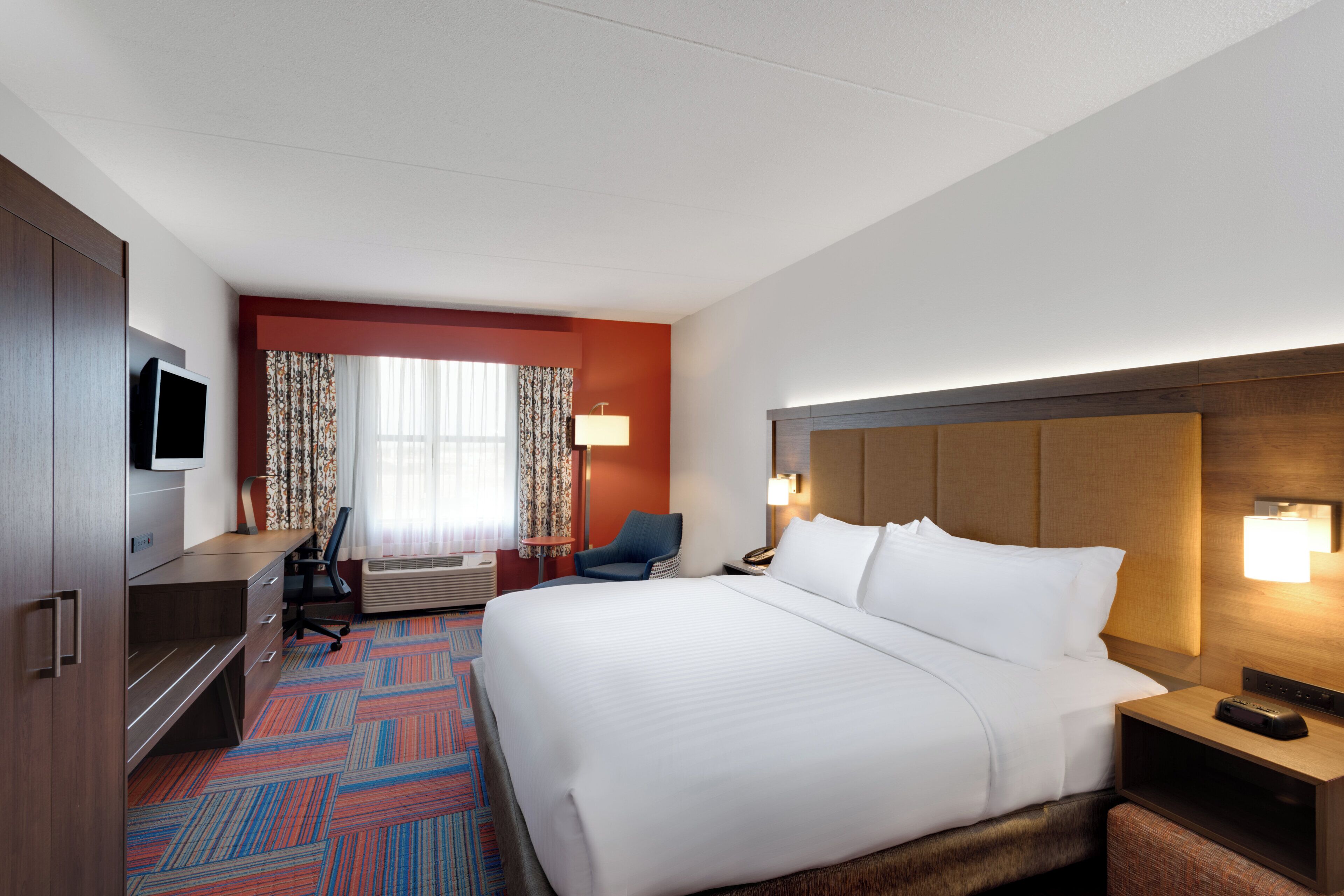 A hotel room with a bed, desk, chair, television, and a window with curtains.