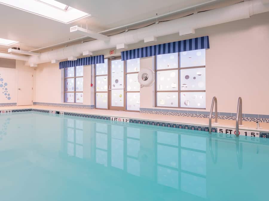 A large indoor swimming pool with clear water, tiled walls, and a ceiling with ventilation ducts.