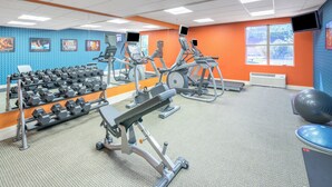A gym with exercise equipment, a mirror, and a wall with exercise posters.