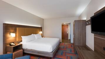 A hotel room with a large bed, a desk with a phone, a flat-screen TV, and a patterned carpet.