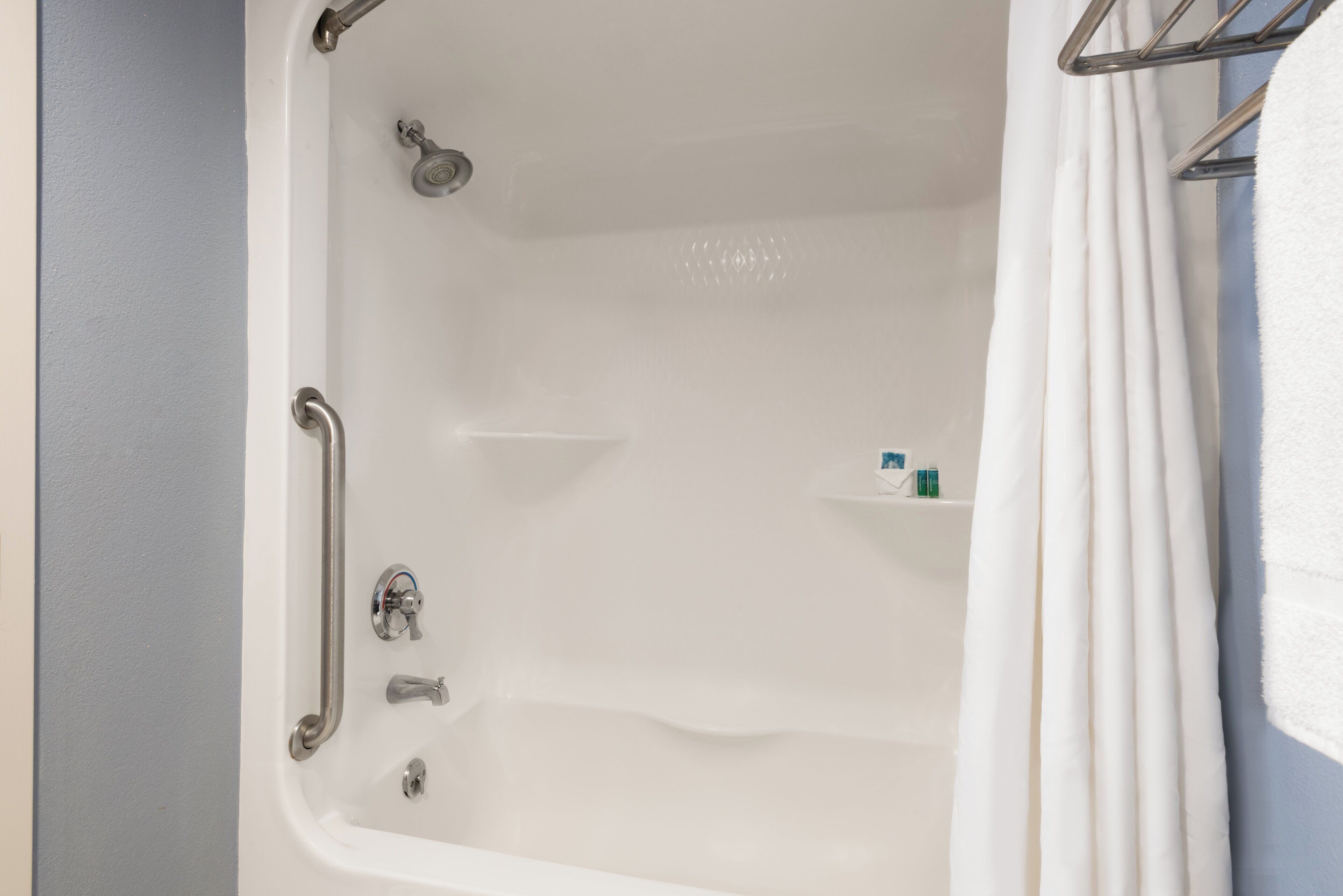 A bathtub with a showerhead, grab bars, and a shelf with toiletries.