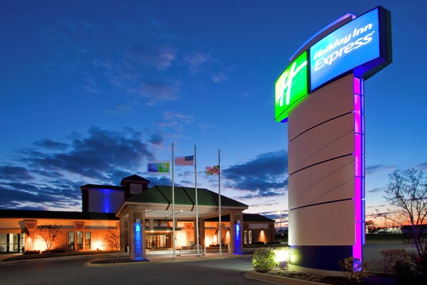 A Holiday Inn Express hotel with a prominent illuminated sign, a flagpole with flags, and a well-lit entrance.