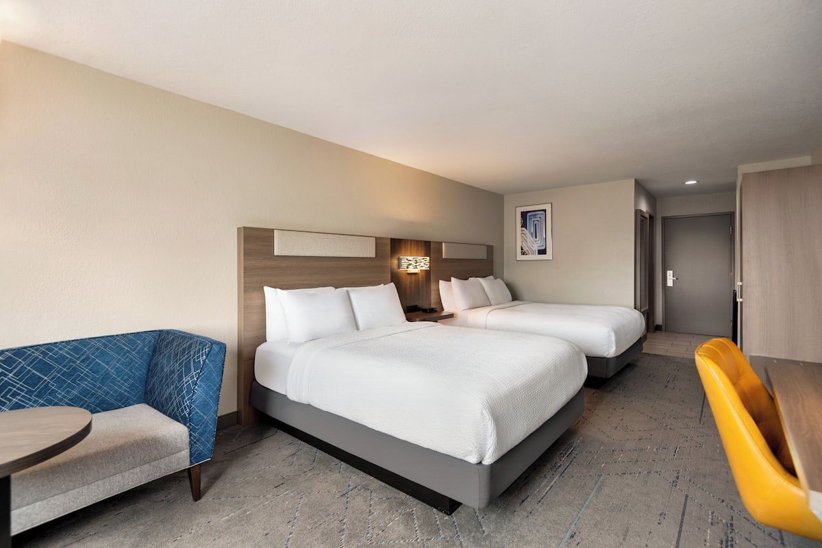A hotel room with two beds, a sofa, a desk, and a chair.