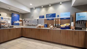 Uma área de café da manhã moderna com estação de autosserviço, incluindo cereais, frutas e um dispensador de bebidas.