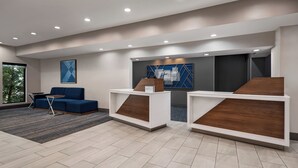 A modern reception area with a blue sofa, two wooden reception desks, and a large window providing natural light. - Holiday Inn Express Morgantown by IHG (Morgantown)