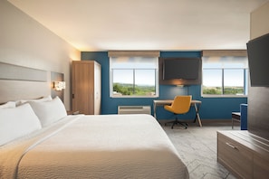 A hotel room with a large bed, a desk, a chair, a television, and a view of the outdoors. - Holiday Inn Express Morgantown by IHG (Morgantown)