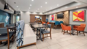 A modern dining area with multiple tables and chairs, a long bench, and a TV mounted on the wall. - Holiday Inn Express Morgantown by IHG (Morgantown)