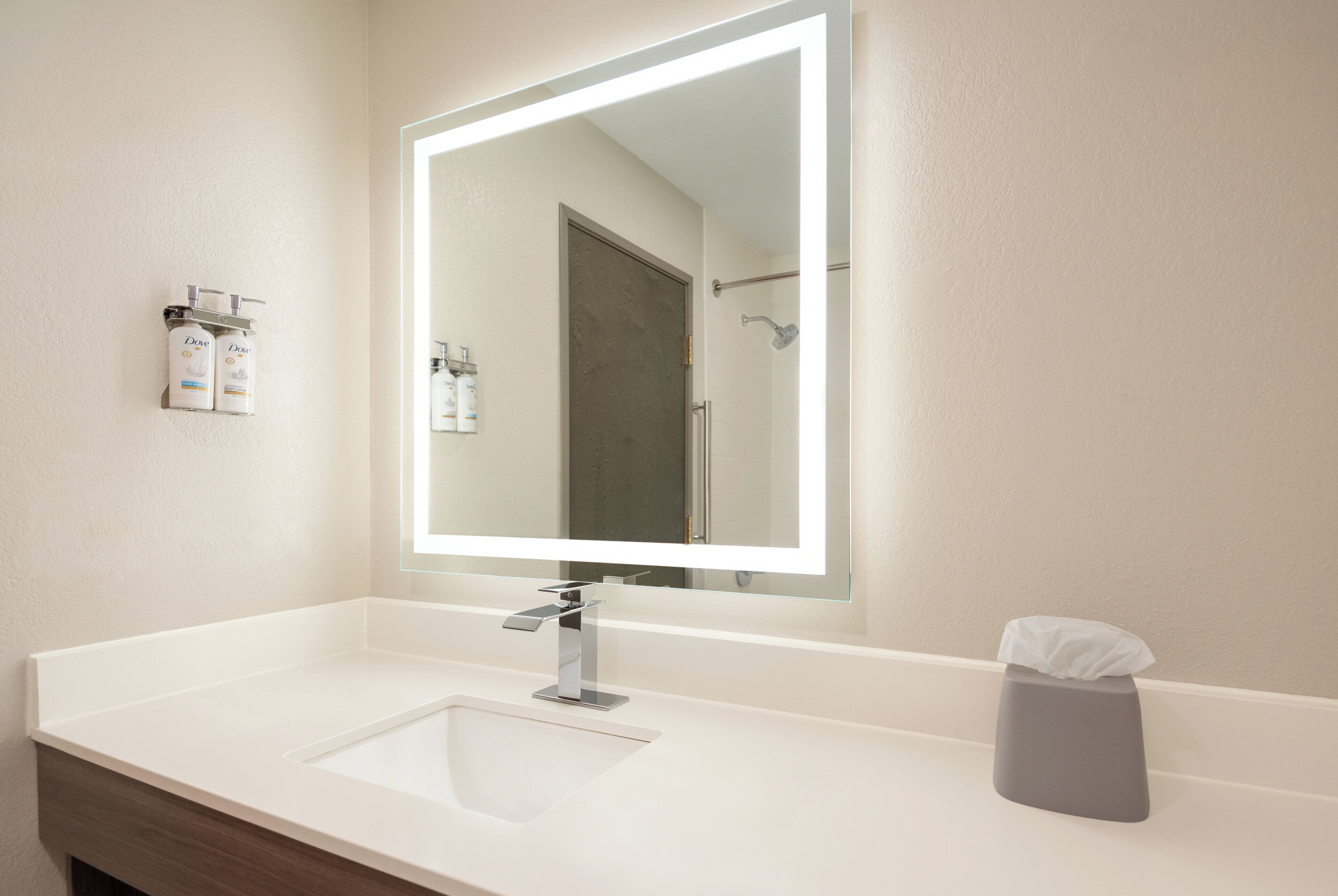 A modern bathroom with a white sink, a large mirror, and a towel dispenser.