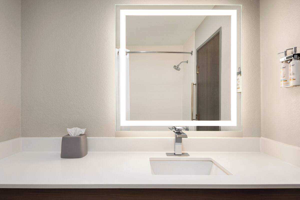 A modern bathroom with a large mirror, a shower, and a white sink.