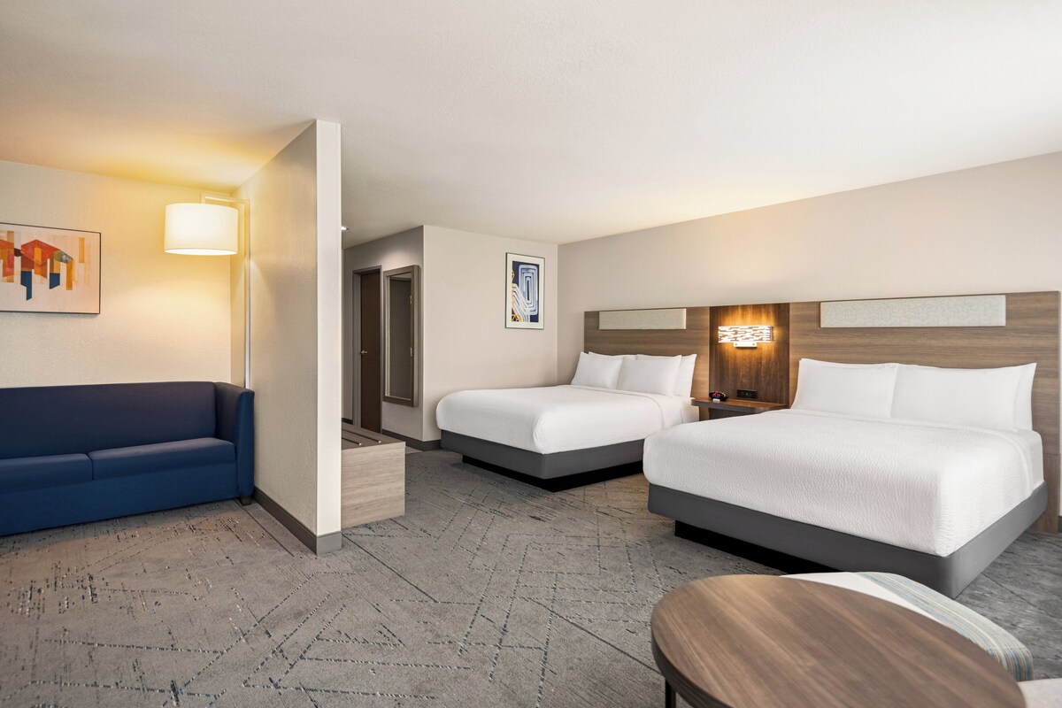 Ein Hotelzimmer mit einem blauen Sofa, zwei Einzelbetten, einem Holztisch und einer Wandlampe.