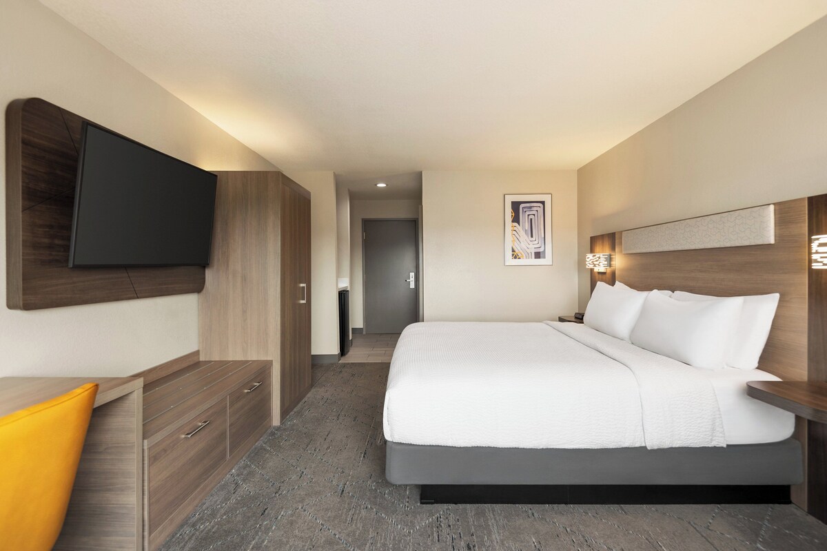 Ein modernes Hotelzimmer mit einem großen Bett, einem Holzschrank und einem flachbildfernseher an der Wand.