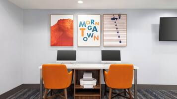 A modern office space with two desks, each with a computer monitor, and two orange chairs. There are three framed artworks on the wall above the desks.