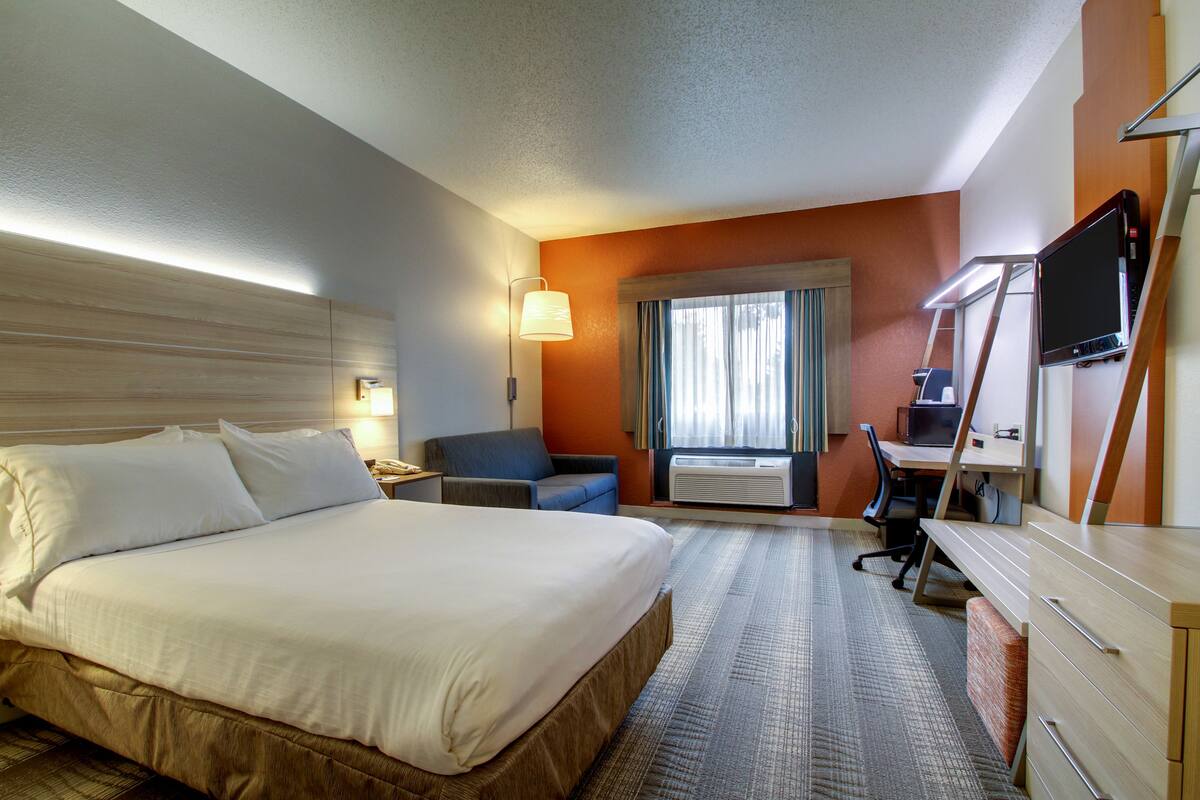 A hotel room with a large bed, a desk, a chair, and a TV.