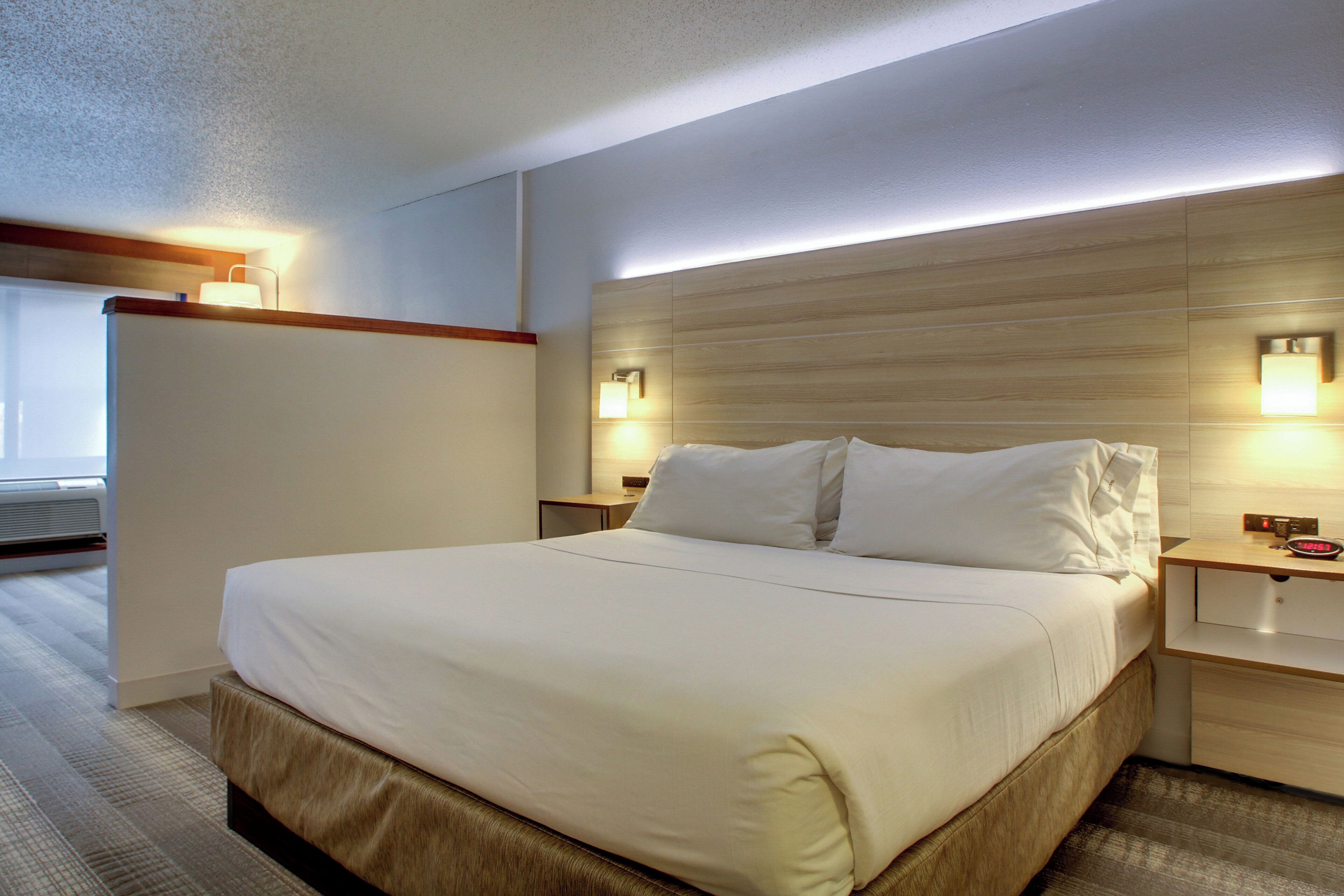 A hotel room with a large bed, two bedside tables, a nightstand, and a wall-mounted light fixture.