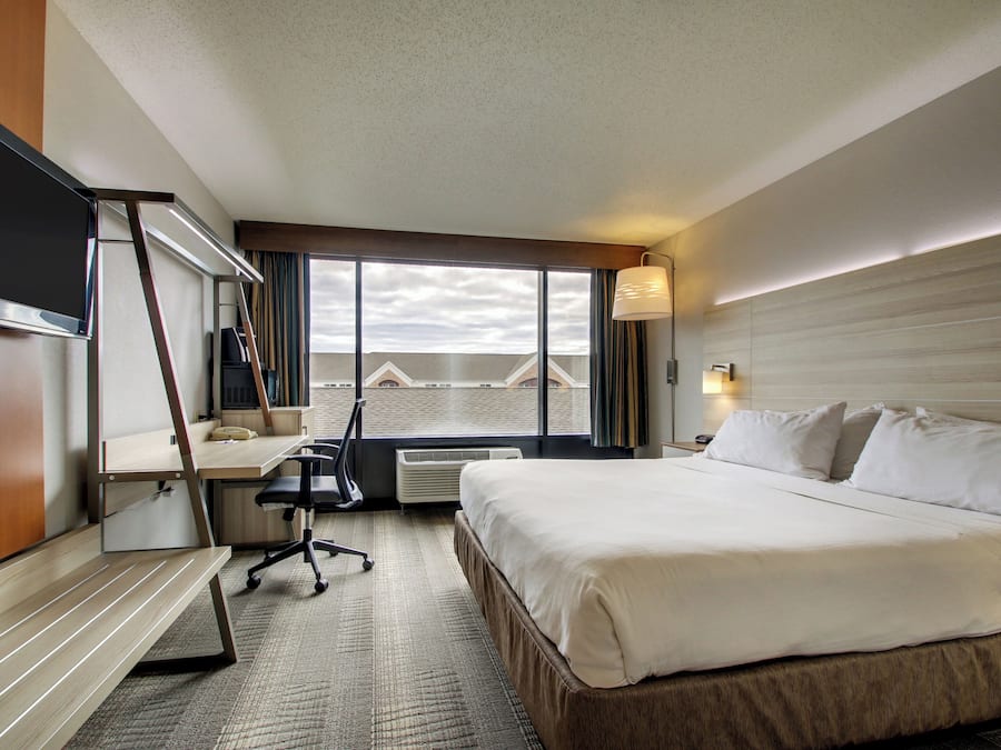 Habitación de hotel con cama, escritorio, silla y ventana grande con vistas.