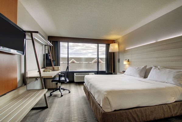 A hotel room with a bed, desk, chair, and a large window with a view. - Holiday Inn Express Milwaukee North Brown Deer/Mequon by IHG (Milwaukee)
