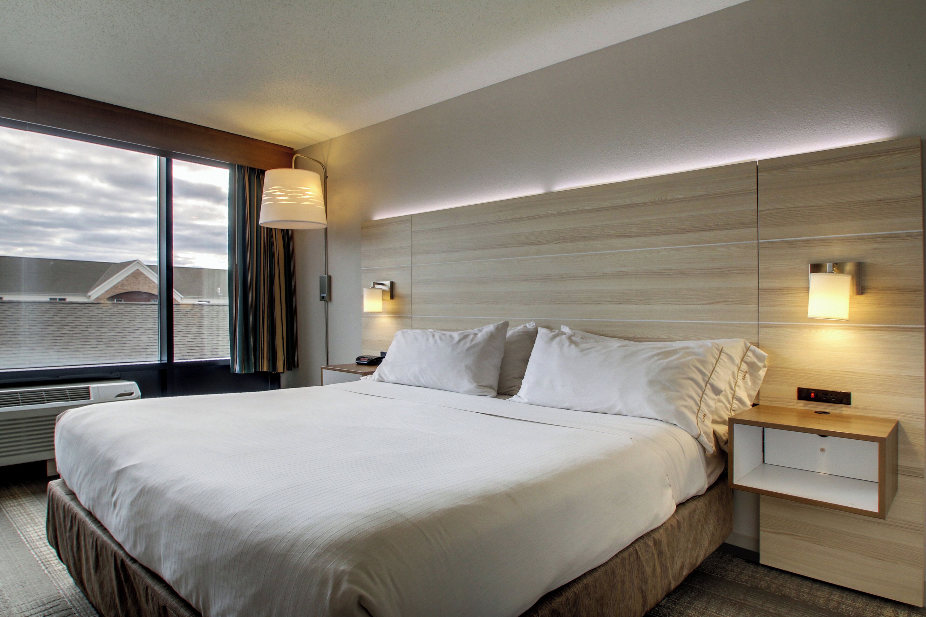 Une chambre d’hôtel avec un grand lit, des tables de chevet, une fenêtre avec des rideaux et une vue sur les bâtiments environnants.